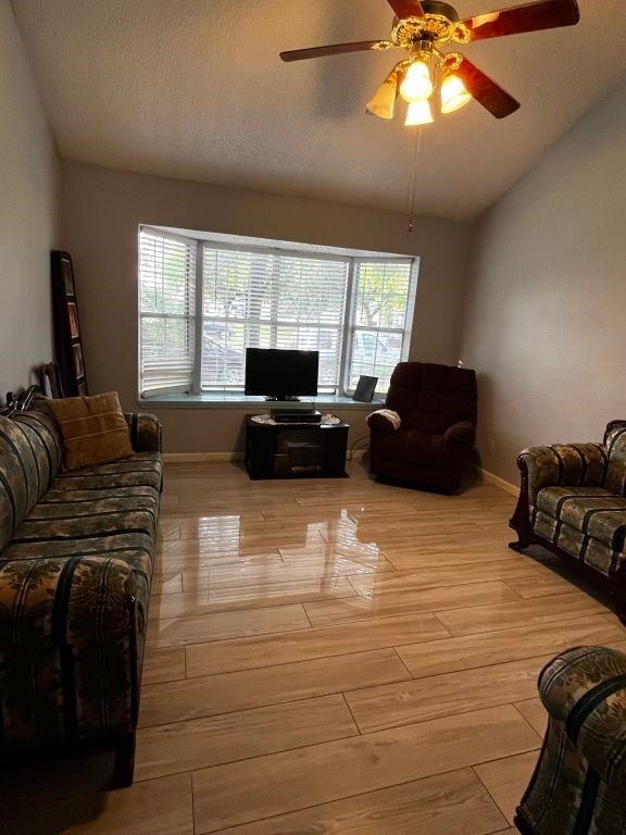 living area with vaulted ceiling, light wood-style floors, healthy amount of natural light, ceiling fan, and baseboards