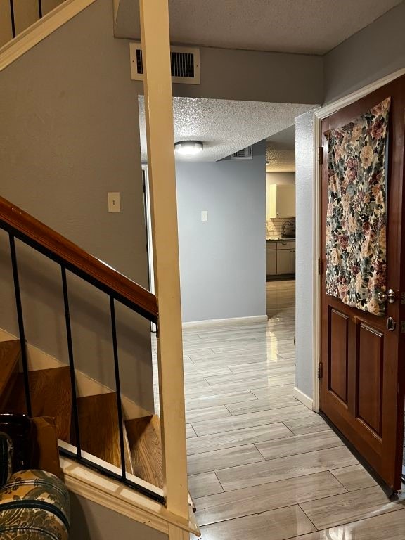 entryway with light wood-style floors, a textured ceiling, and baseboards