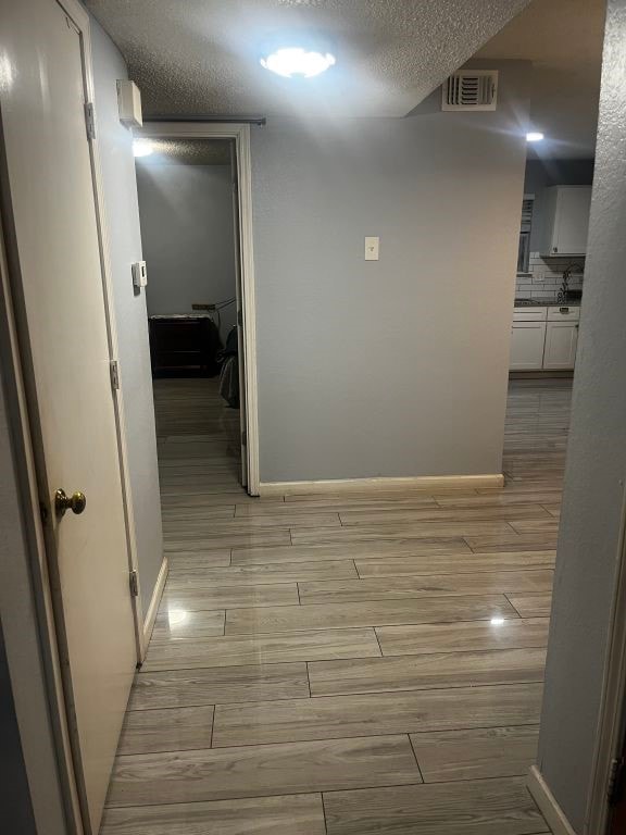 hallway with light wood-style floors, baseboards, and a textured ceiling