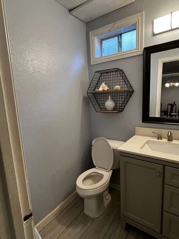 half bath with toilet, wood finished floors, vanity, and baseboards