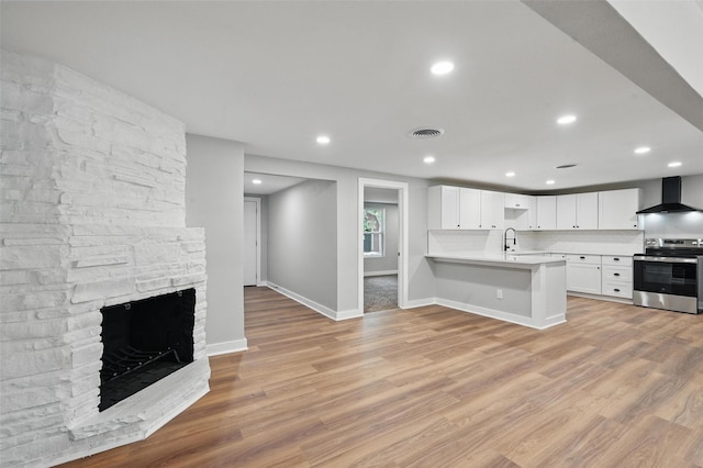 1220 Brittany Ln, Arlington, TX 76013 - kitchen featuring stainless steel range with electric stovetop, wall chimney exhaust hood, a peninsula, light countertops, and light wood-style flooring