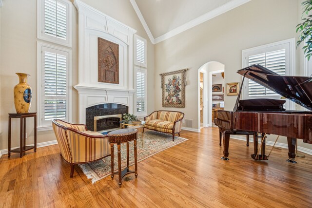 4024 Oakmeadow Dr, Plano, TX 75093 - living room featuring crown molding, high vaulted ceiling, a fireplace, arched walkways, and light wood-style flooring