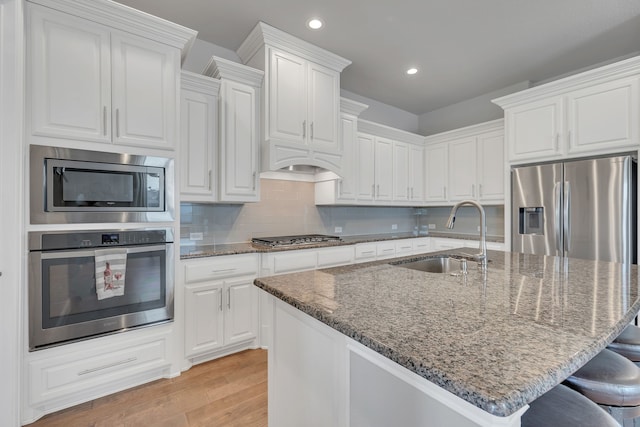 14937 Belclaire Ave, Aledo, TX 76008 - kitchen featuring appliances with stainless steel finishes, a sink, a breakfast bar, light wood-style flooring, and white cabinetry