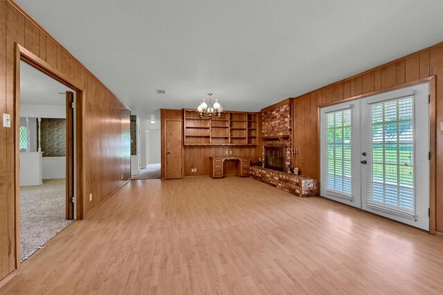 unfurnished living room featuring wooden walls, a chandelier, light wood-type flooring, a fireplace, and built in shelves