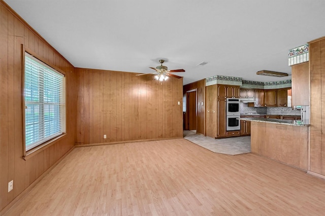 unfurnished living room with light wood finished floors, a ceiling fan, and wood walls