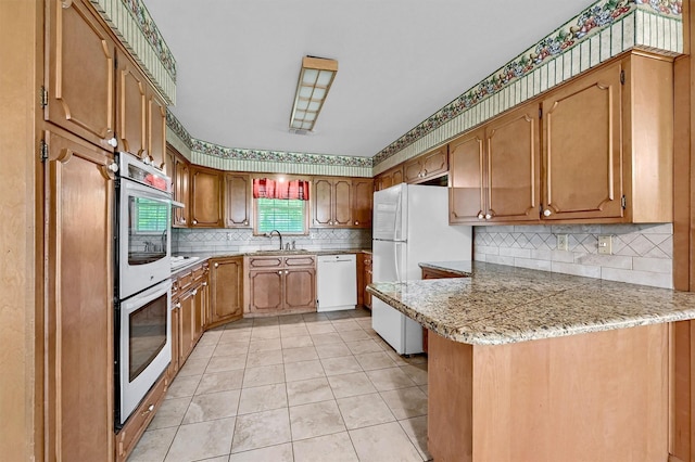 kitchen with white appliances, a peninsula, decorative backsplash, a sink, and light countertops