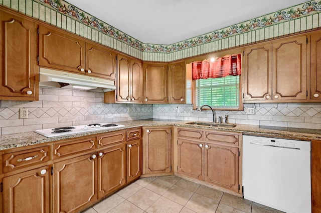 kitchen with white appliances, a sink, under cabinet range hood, light tile patterned flooring, and brown cabinetry