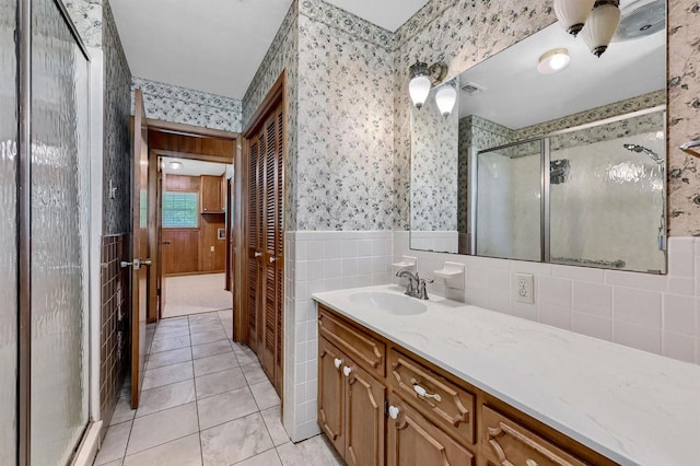 full bathroom with wallpapered walls, a shower stall, vanity, tile patterned flooring, and a wainscoted wall