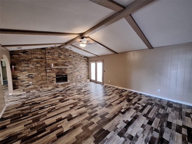 unfurnished living room featuring ceiling fan, wood finished floors, a brick fireplace, baseboards, and arched walkways