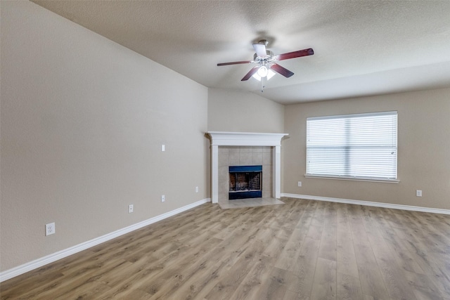 5844 Sunny Meadow Ln, Grand Prairie, TX 75052 - unfurnished living room with light wood-style floors, a ceiling fan, a tiled fireplace, baseboards, and a textured ceiling