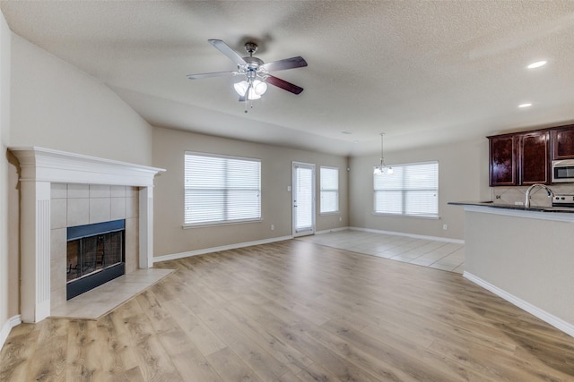 5844 Sunny Meadow Ln, Grand Prairie, TX 75052 - unfurnished living room with a ceiling fan, a tile fireplace, light wood-style flooring, a textured ceiling, and baseboards