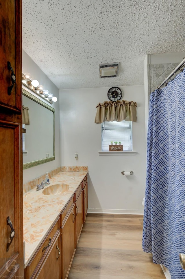 full bath featuring wood finished floors, a textured ceiling, vanity, baseboards, and a shower with shower curtain