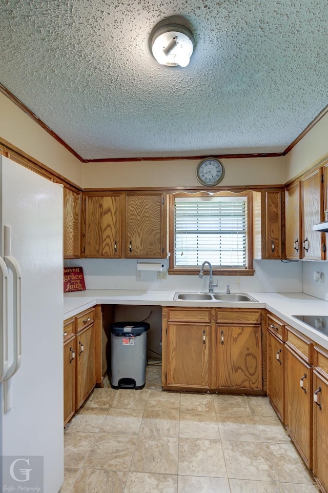 kitchen with freestanding refrigerator, a sink, black electric cooktop, a textured ceiling, and brown cabinets