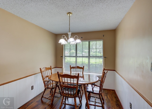 dining area with dark wood-type flooring, a chandelier, wainscoting, and a textured ceiling