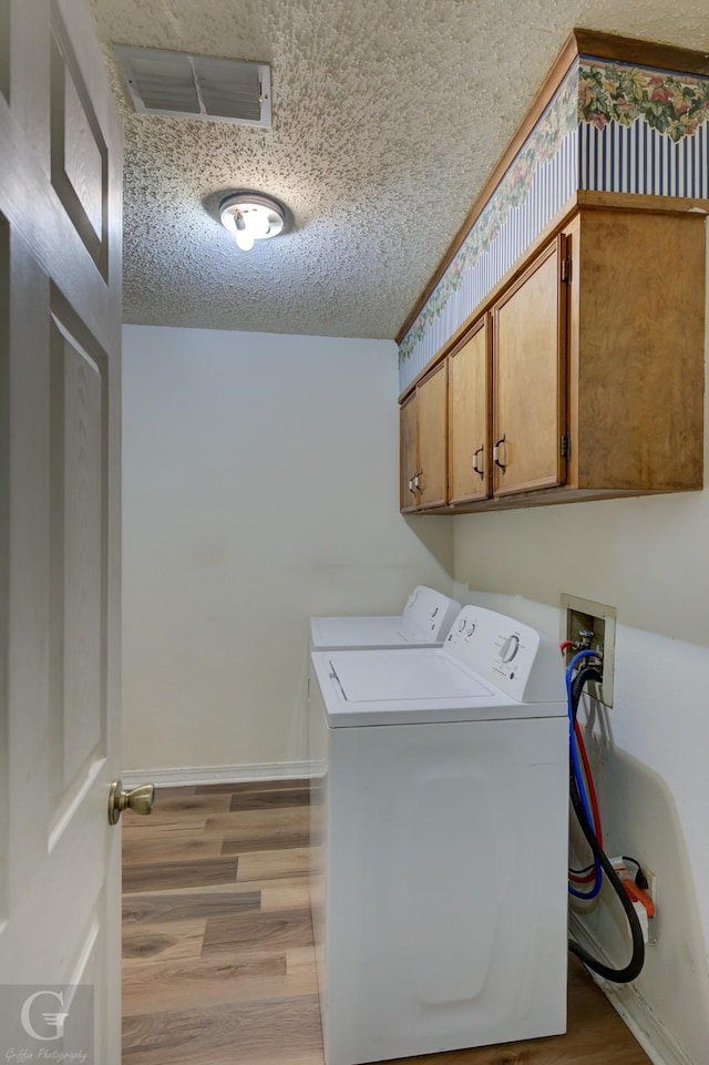 laundry area featuring washing machine and dryer, light wood-type flooring, a textured ceiling, cabinet space, and baseboards
