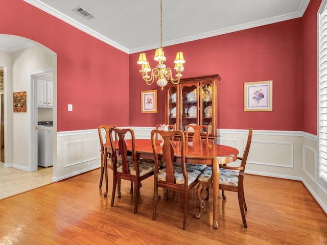 1457 Susan Ln, Carrollton, TX 75007 - dining space featuring arched walkways, washer / clothes dryer, light wood finished floors, ornamental molding, and a chandelier