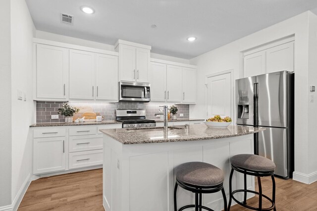 2606 High Cotton Ln, Garland, TX 75042 - kitchen with appliances with stainless steel finishes, a sink, light wood-style flooring, white cabinetry, and a kitchen breakfast bar
