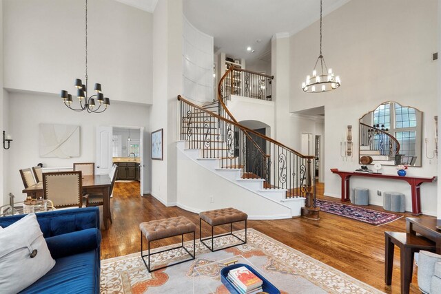 living room featuring a chandelier, a towering ceiling, stairs, wood finished floors, and baseboards