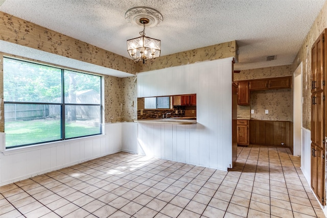 104 NE Rosamond St, Burleson, TX 76028 - kitchen with brown cabinetry, a chandelier, wallpapered walls, a textured ceiling, and wainscoting