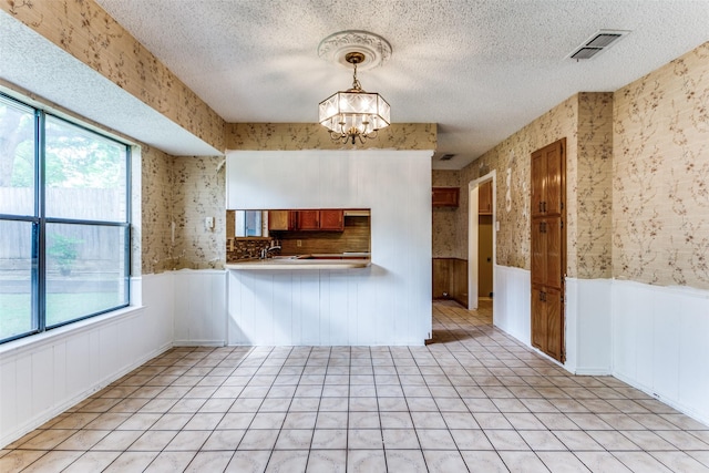 104 NE Rosamond St, Burleson, TX 76028 - kitchen featuring brown cabinets, a wainscoted wall, healthy amount of natural light, a chandelier, and wallpapered walls