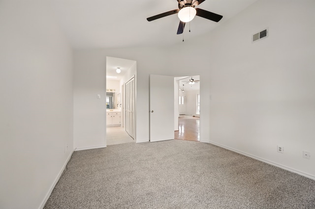 unfurnished bedroom featuring light colored carpet, vaulted ceiling, ensuite bath, baseboards, and a closet