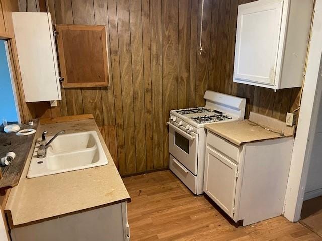 100 E Hill St, Woodson, TX 76491 - kitchen with white range with gas cooktop, a sink, wood walls, light wood-type flooring, and white cabinets