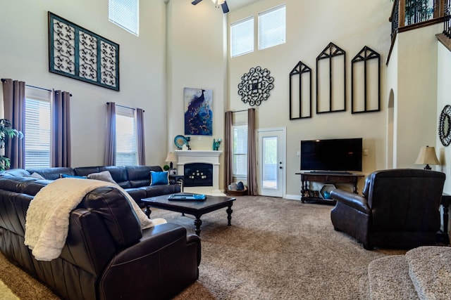 carpeted living room featuring a high ceiling, a ceiling fan, a fireplace, and baseboards