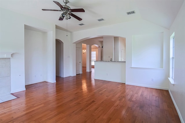 unfurnished living room featuring ceiling fan, arched walkways, wood finished floors, baseboards, and vaulted ceiling