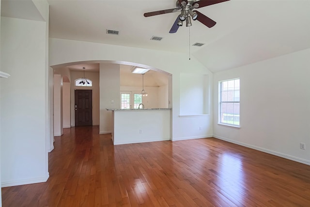 unfurnished living room featuring ceiling fan, arched walkways, vaulted ceiling, wood-type flooring, and baseboards