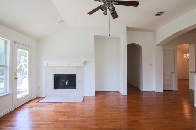 unfurnished living room featuring a ceiling fan, vaulted ceiling, light wood-type flooring, arched walkways, and a fireplace