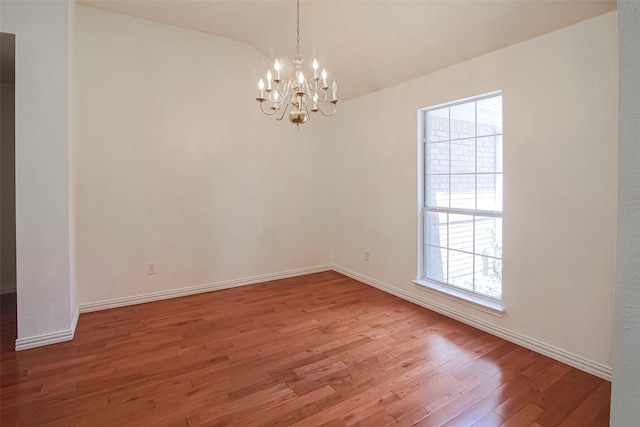 spare room with a chandelier, wood finished floors, baseboards, and vaulted ceiling