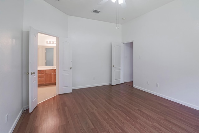 unfurnished bedroom featuring dark wood-style floors, baseboards, connected bathroom, a ceiling fan, and a high ceiling