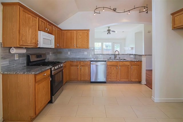 kitchen with appliances with stainless steel finishes, a sink, ceiling fan, dark stone counters, and tasteful backsplash