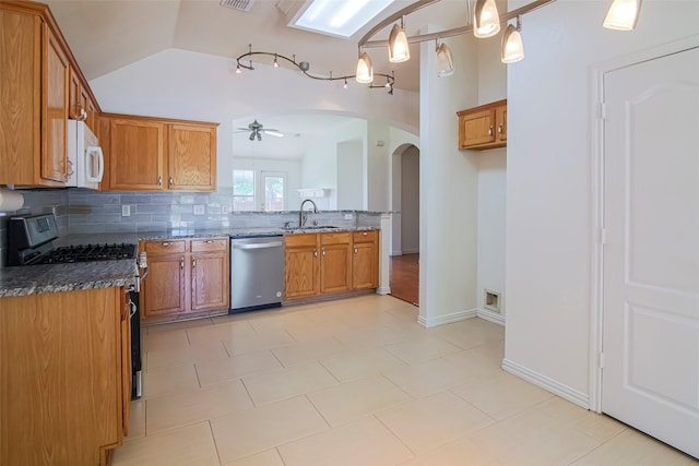 kitchen featuring appliances with stainless steel finishes, arched walkways, a sink, brown cabinetry, and lofted ceiling