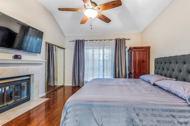 bedroom featuring vaulted ceiling, wood finished floors, a fireplace, ceiling fan, and baseboards