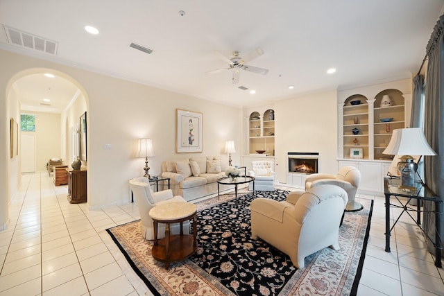 living area featuring arched walkways, ceiling fan, light tile patterned flooring, built in features, and crown molding