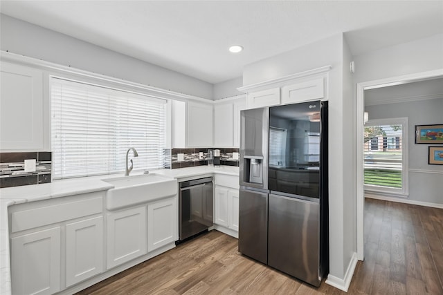 kitchen with stainless steel appliances, a sink, white cabinets, backsplash, and wood finished floors