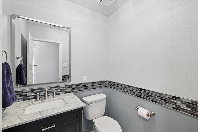 half bathroom with toilet, vanity, tile walls, and decorative backsplash