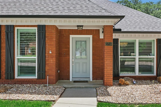 entrance to property with a shingled roof and brick siding