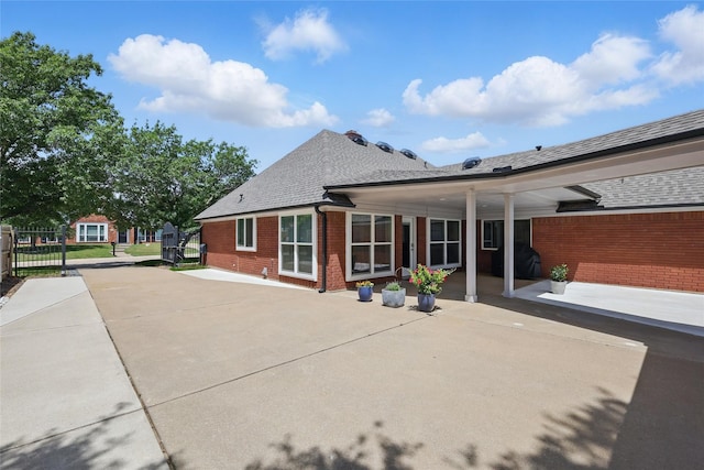 rear view of property featuring fence, brick siding, and a shingled roof