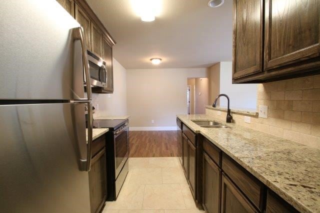 8036 Doreen Ave, Fort Worth, TX 76116 - kitchen featuring stainless steel appliances, a sink, light stone countertops, baseboards, and dark brown cabinets