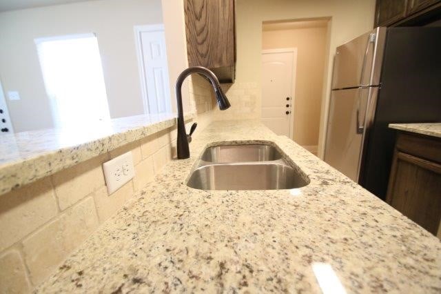 8036 Doreen Ave, Fort Worth, TX 76116 - kitchen featuring a sink, freestanding refrigerator, light stone counters, decorative backsplash, and dark brown cabinetry