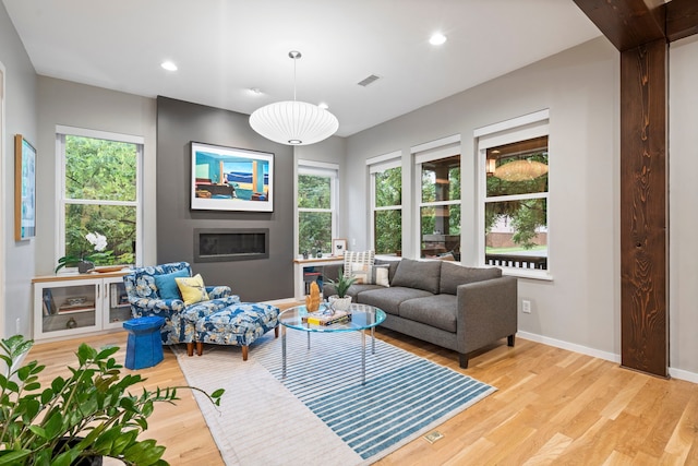 living room with light wood-style floors, plenty of natural light, a glass covered fireplace, baseboards, and recessed lighting