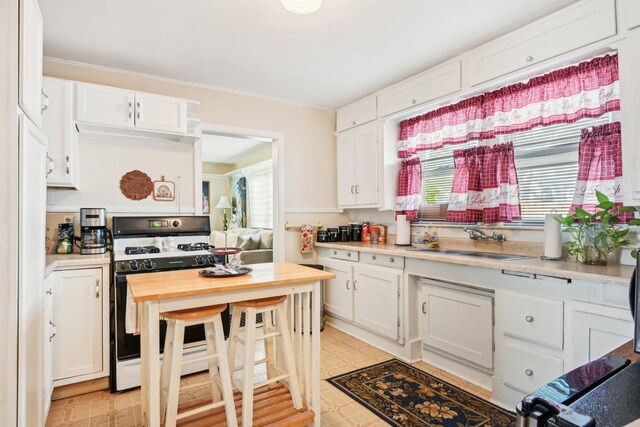 2509 Bird St, Fort Worth, TX 76111 - kitchen with range with gas stovetop, white cabinets, light flooring, and a sink