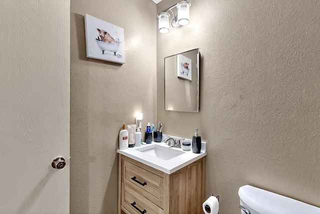 half bathroom featuring toilet, vanity, and a textured wall