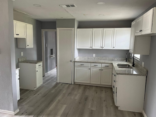 2836 Modree Ave, Dallas, TX 75216 - kitchen with a sink, stone countertops, light wood-type flooring, and white cabinetry