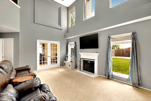 living room featuring a high ceiling, french doors, carpet floors, a fireplace with raised hearth, and plenty of natural light
