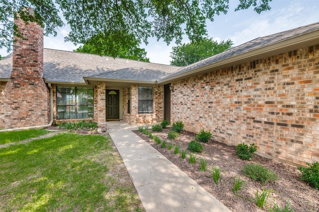 2005 Parkside Dr, Denton, TX 76201 - property entrance featuring a chimney, a shingled roof, brick siding, and a lawn