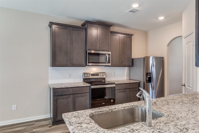 412 Lowery Oaks Trl, Fort Worth, TX 76120 - kitchen featuring appliances with stainless steel finishes, a sink, arched walkways, dark brown cabinetry, and tasteful backsplash