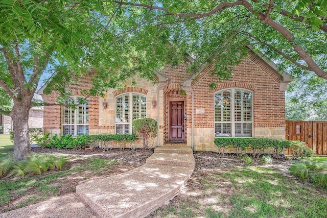 view of front of house with brick siding, fence, and stone siding